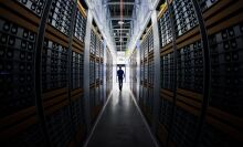 A man in silhouette, walking through racks of computers in a data center.